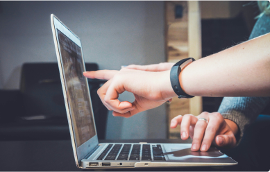 A person pointing on the screen of a laptop with another person scrolling on the laptop's trackpad